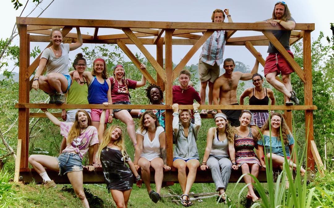 A group of young people posed across a timber frame structure outdoors